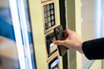 Hand hält Mobiltelefon an Kassenautomat zur bargeldlosen Bezahlung