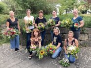 Acht Studierende stehen bzw. sitzen im Außenbereich und präsentieren ihre Blumensträuße