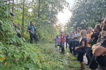 Ein Mann steht vor einem Baum im Wald und spricht zu einer Gruppe von Menschen