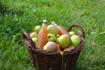 Äpfel und Flaschen in einem Korb auf einer Wiese.