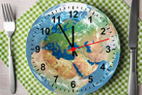 Telleruhr mit Weltkarte, die 5 vor 12 Uhr anzeigt; daneben Besteck © Opus