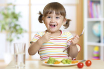 Kleines Mädchen mit Zöpfen hält Gabel in der Hand und isst Gemüse © Thinkstock