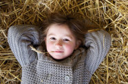 Mädchen hat Getreidehalm im Mund und liegt im Stroh. © mimagephotos – stock.adobe.com
