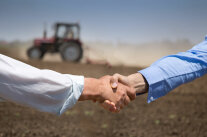 Handschlag zweier Personen auf einem Feld vor einem Traktor